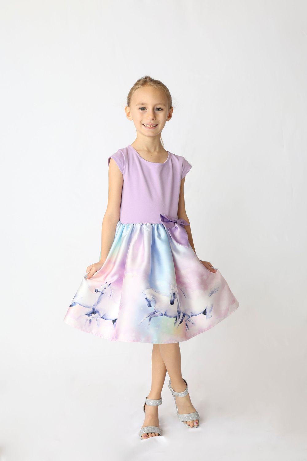 A child wearing a sleeveless lavender dress with a watercolor-style floral skirt twirls in a white studio setting.