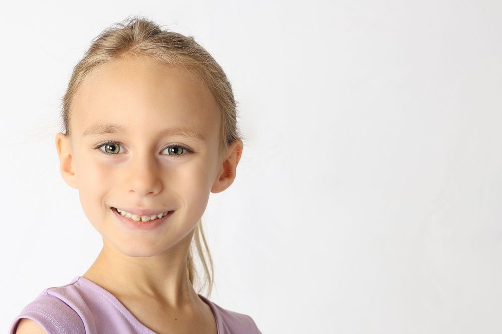 Four smiling children wearing casual clothing pose together against a white background.