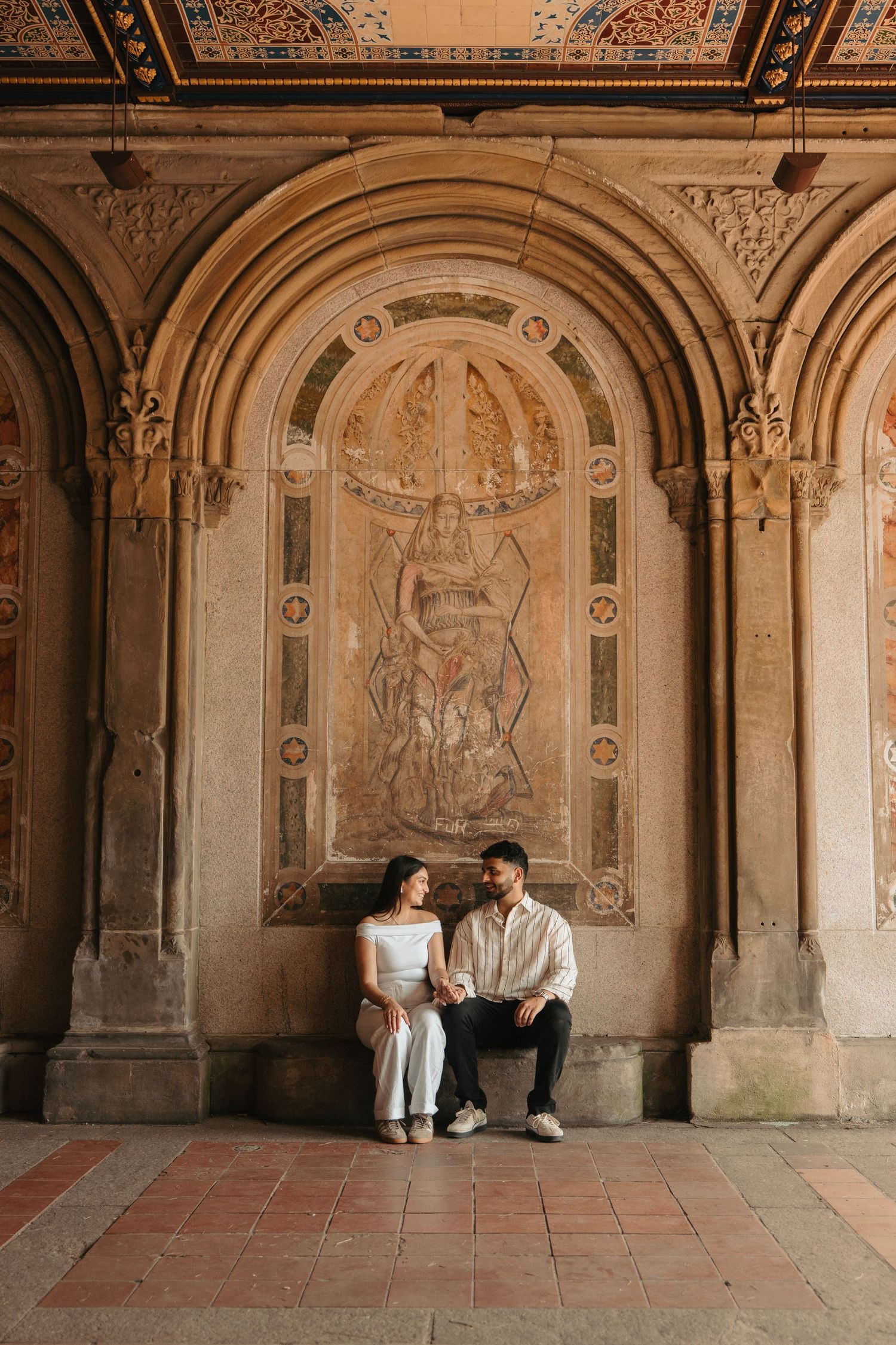 A couple sits beneath ornate architectural arches during their engagement session.