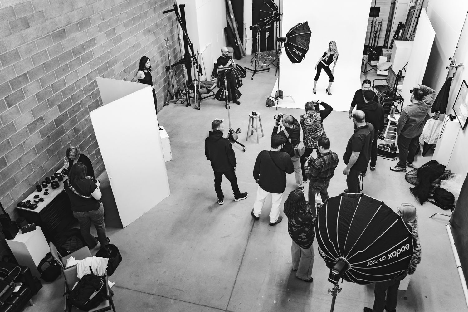 People gather in a modern building hallway or gallery space with white walls and brick flooring.