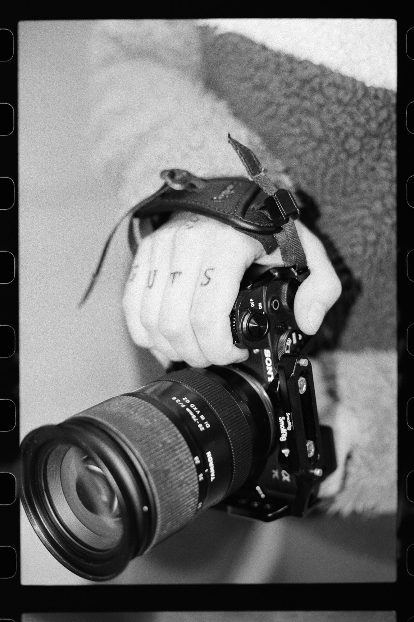 A black and white photo of a camera with a telephoto lens being held by a gloved hand.