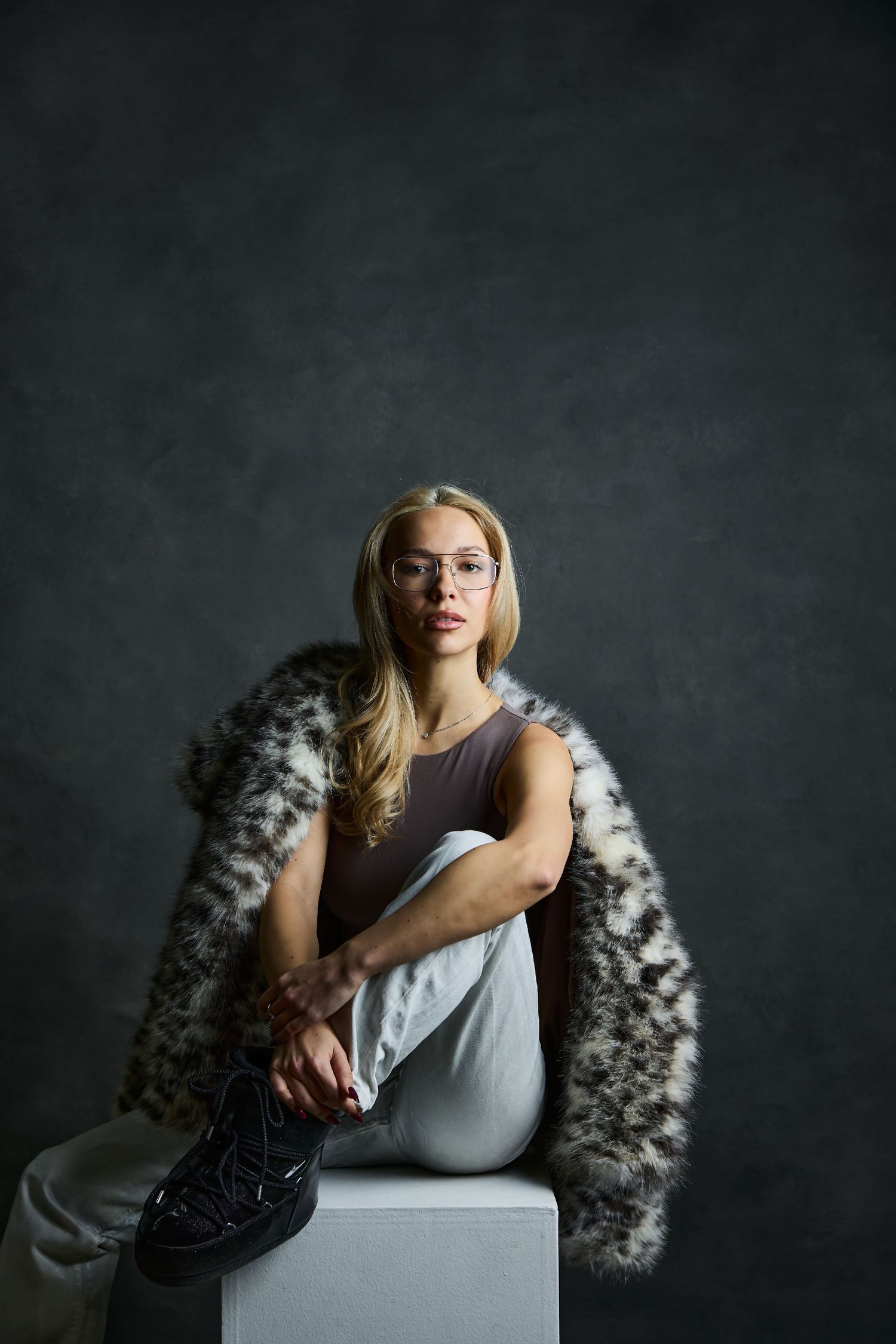 A moody portrait series showing a figure in a white tank top reclining on a dark chair against a dramatic gray backdrop.