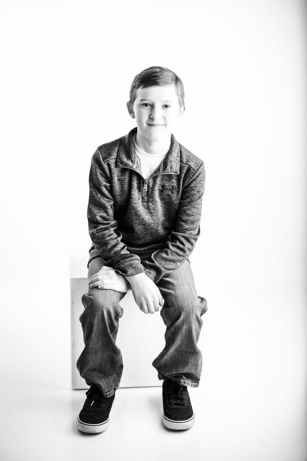 Black and white portrait series of a child sitting casually on white background in casual clothing.