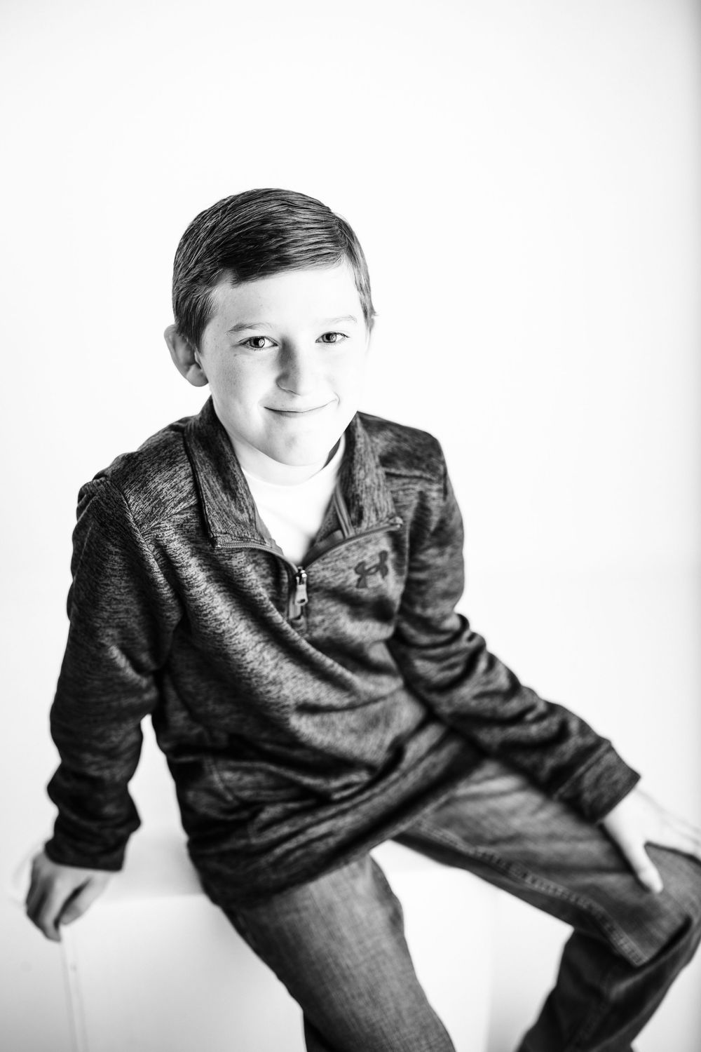 Black and white portrait of a young child wearing a dark sweater and jeans against a white background.