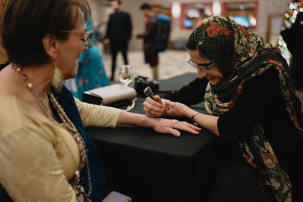 A woman applies intricate henna mehndi design on a guests hand at a cultural wedding celebration.