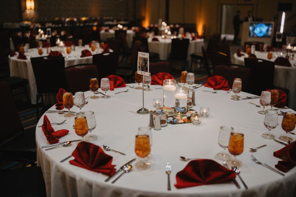 Elegant wedding reception tables with white linens, red napkins, candles, and glassware in a dimly lit ballroom.at Sandia Resort and Casino