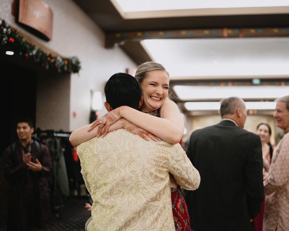 A smiling bride in a gold dress shares a warm hug with a guest at her wedding reception.