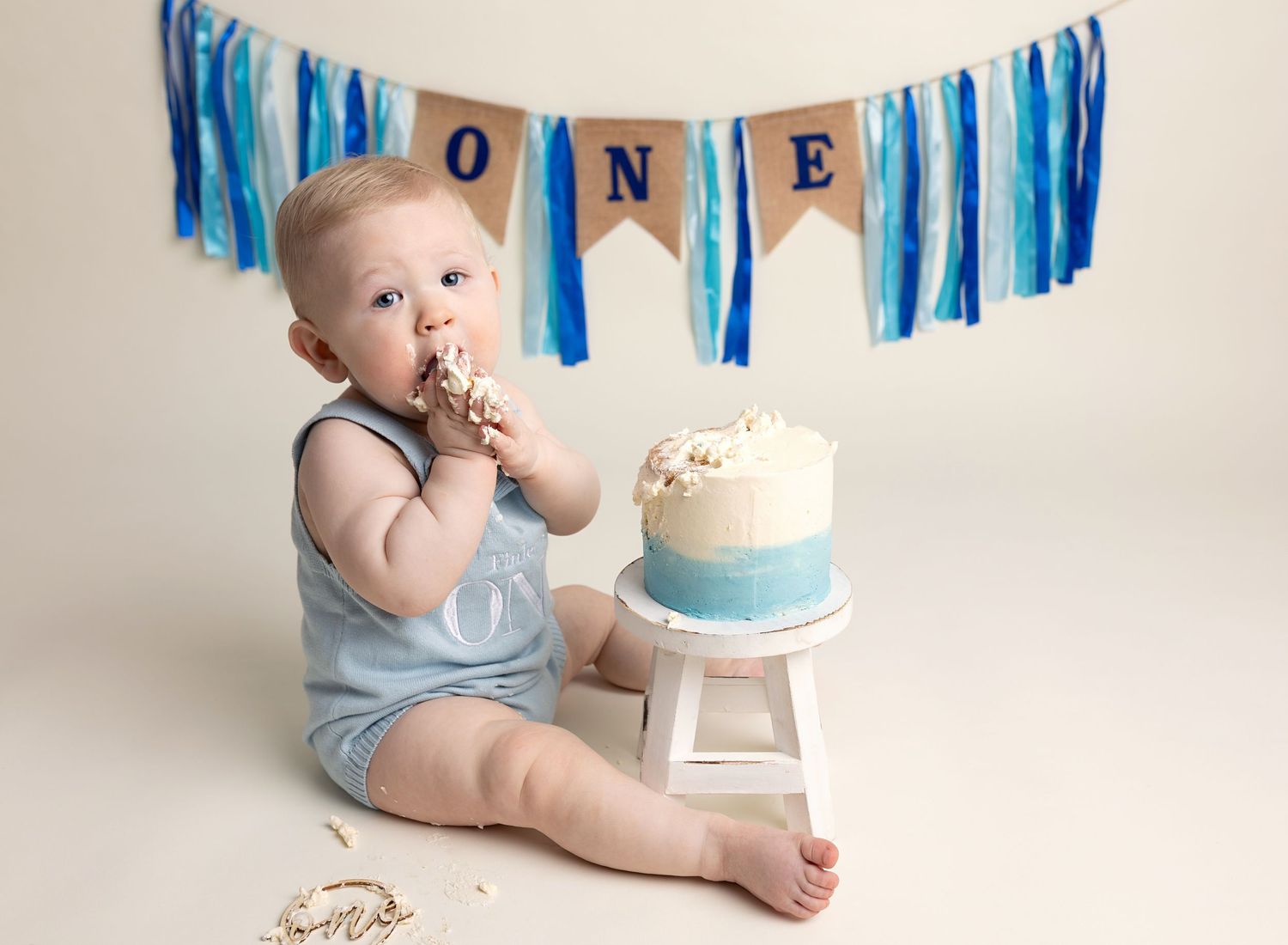 baby boy eating his birthday cake with hands, looking at camera during first birthday cake smash session near Glasgow