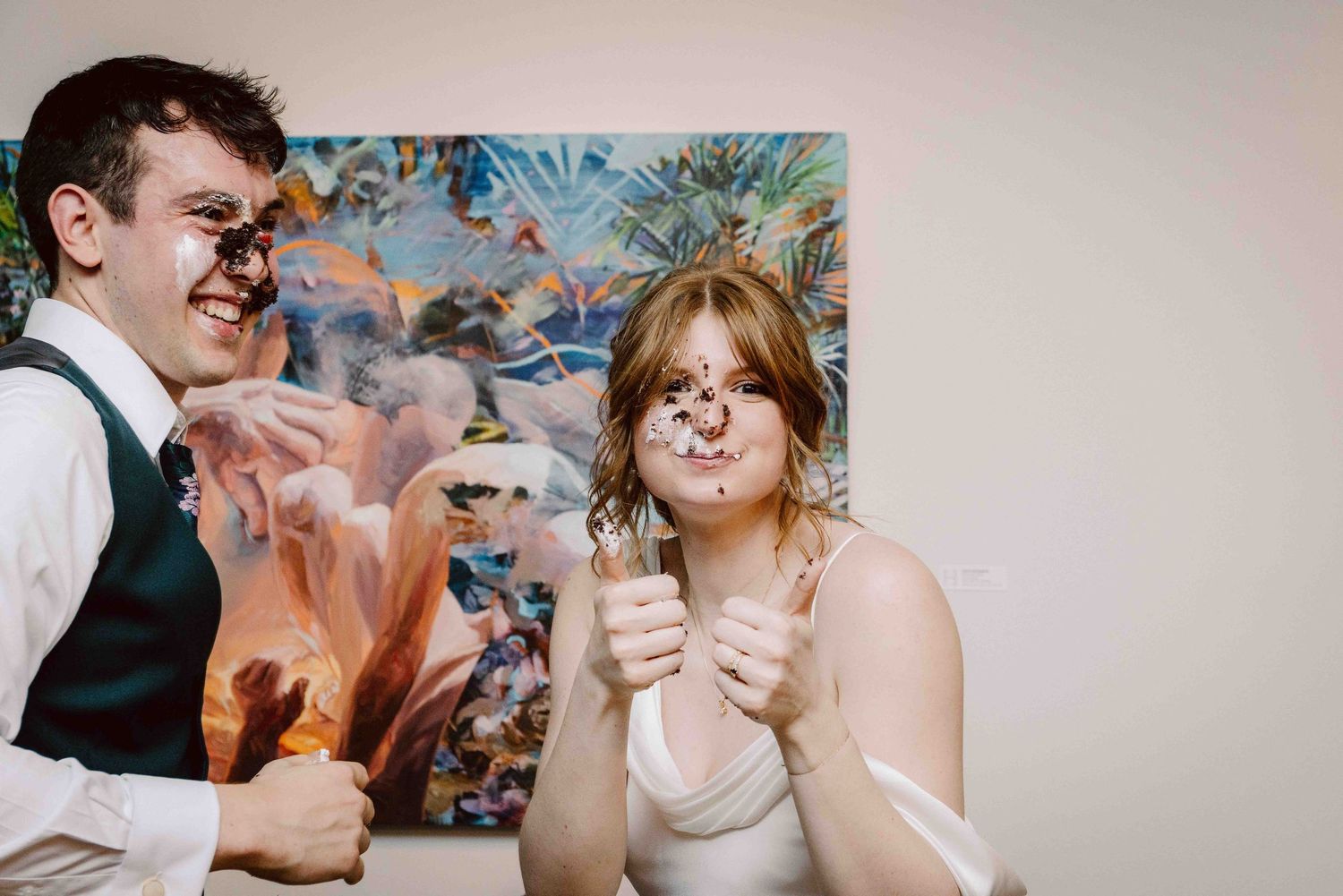 A bride giving the camera a thumb's up right after her and the groom smashed cake in each other's faces.