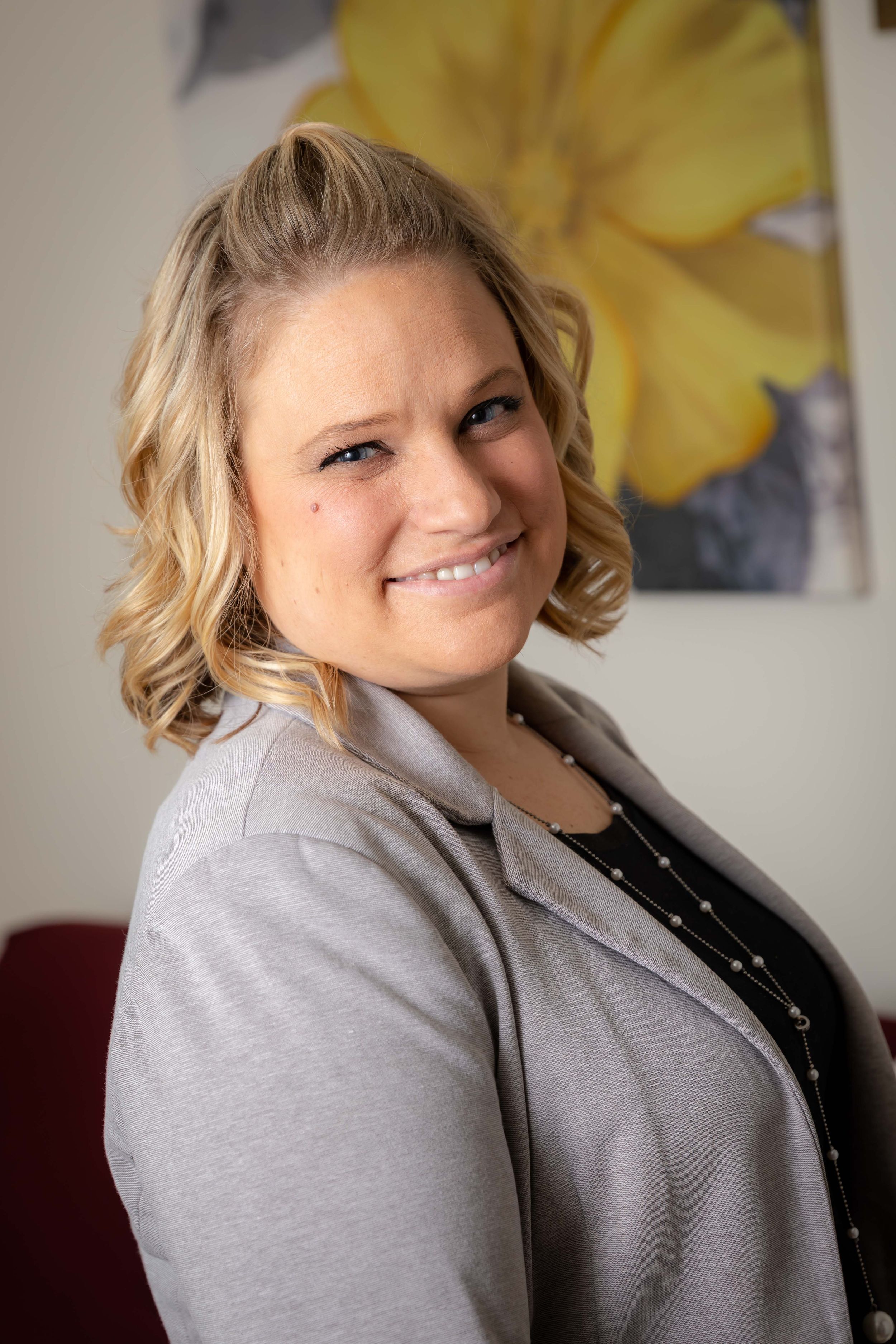 Professional wearing a gray blazer and black top smiles while sitting in an indoor setting.