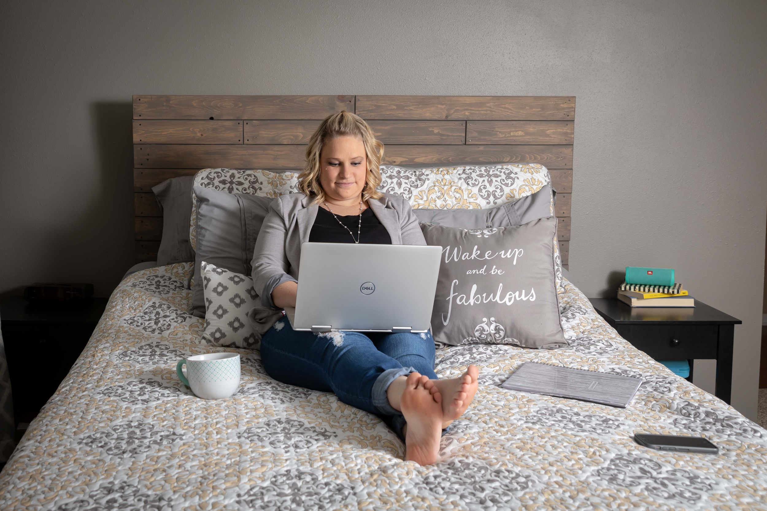 Person working from bed with laptop while surrounded by cozy pillows and blue floral bedding.