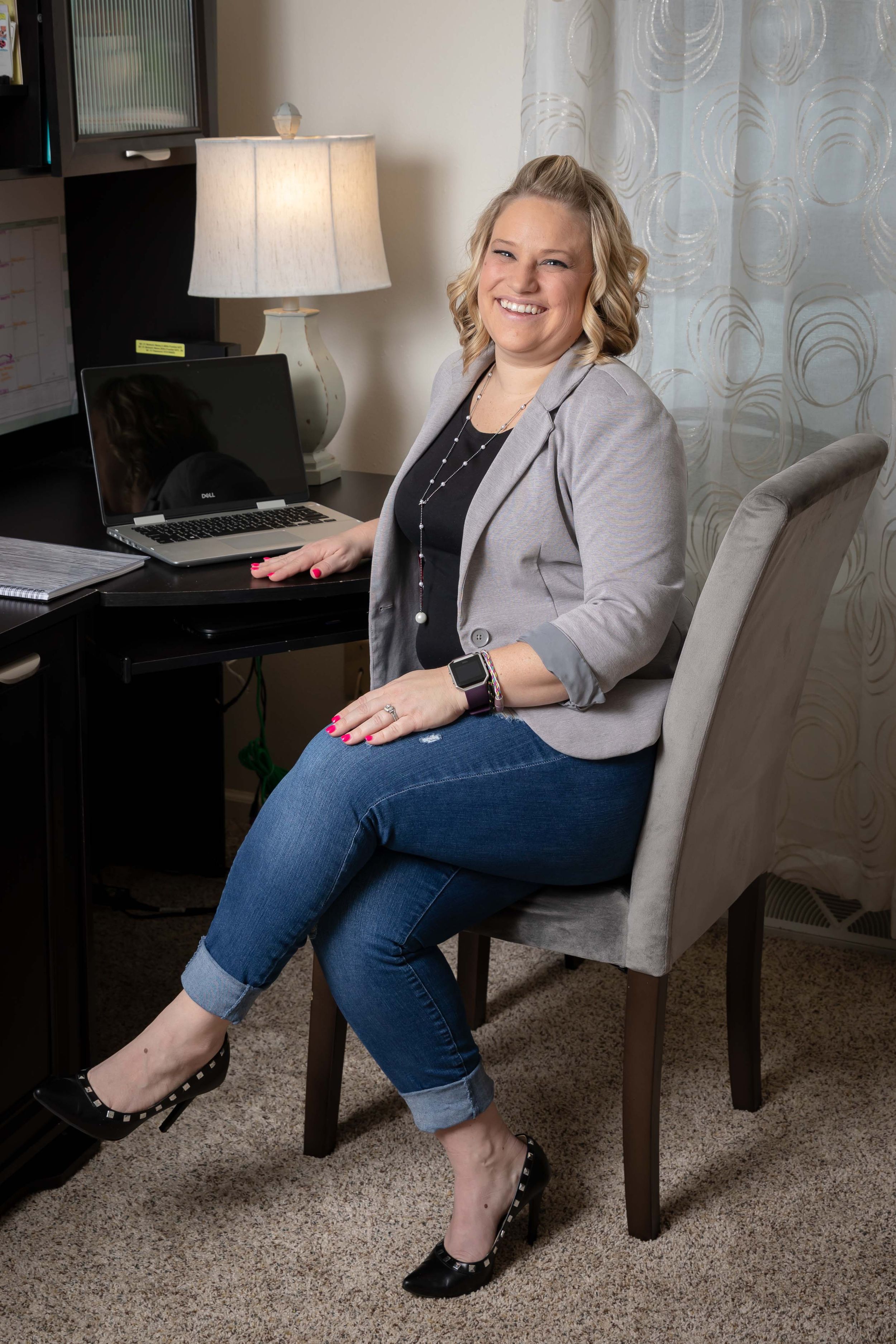 Person smiling while working at home office desk with laptop and table lamp in cozy room setting.