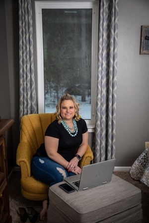Professional working at desk with laptop in home office setting with yellow accent chair and gray curtains.
