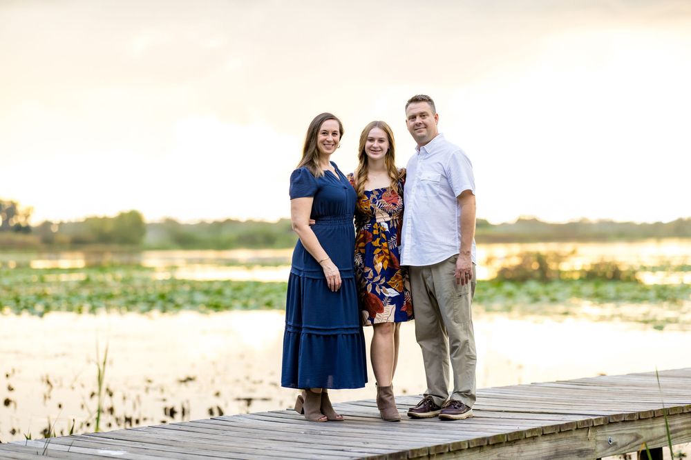 Family poses together on a wooden pier overlooking a scenic beach during sunset.