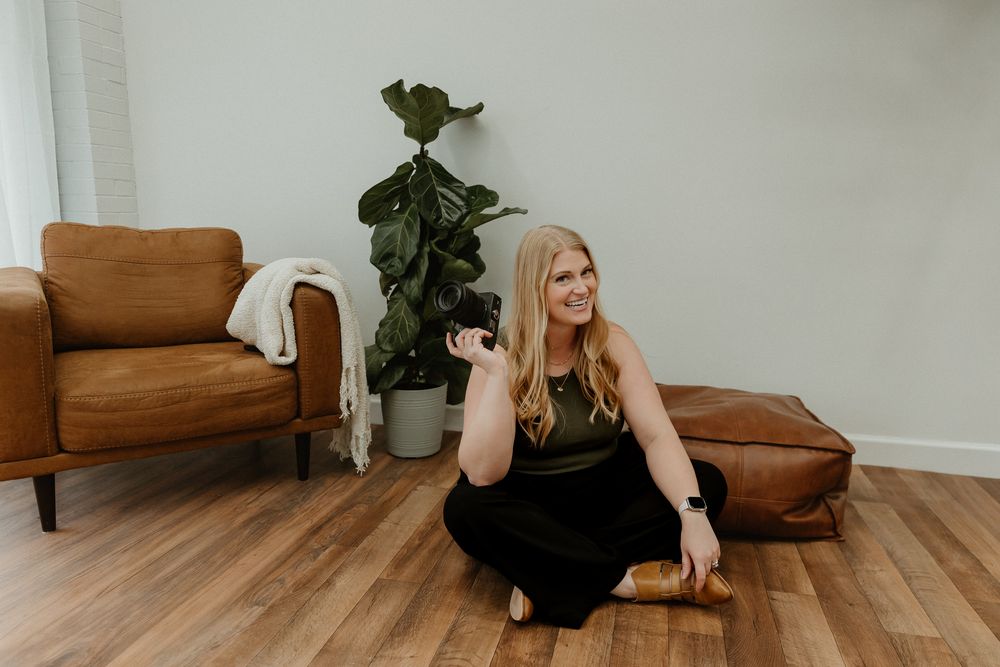Brown leather chair sits in corner of room with hardwood floors and white walls next to potted plant.
