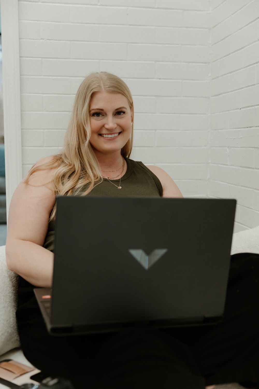 Person working on laptop while sitting on couch in bright white room.