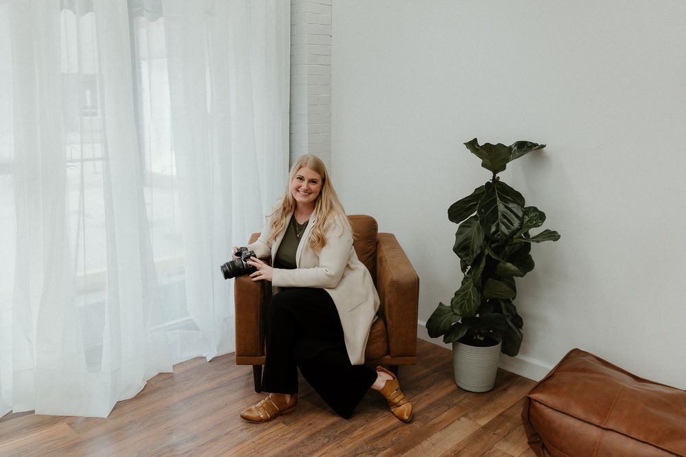 Person sitting on brown leather sofa in bright minimalist room with houseplants and white walls.