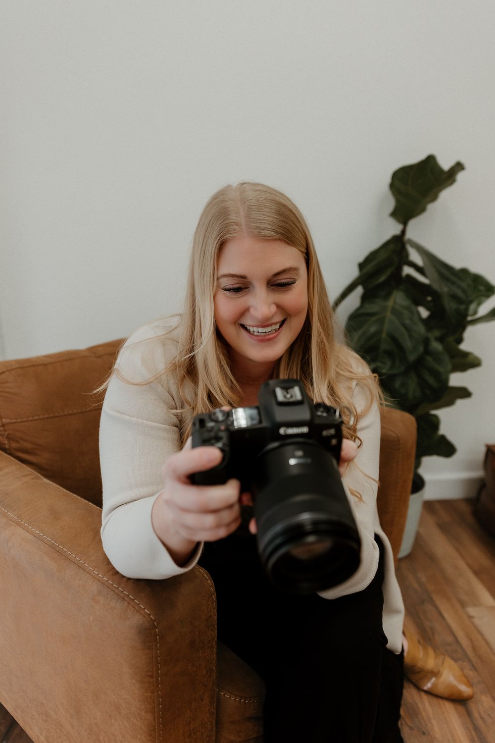 A photographer laughs while reviewing photos on a digital camera while seated on a brown couch.
