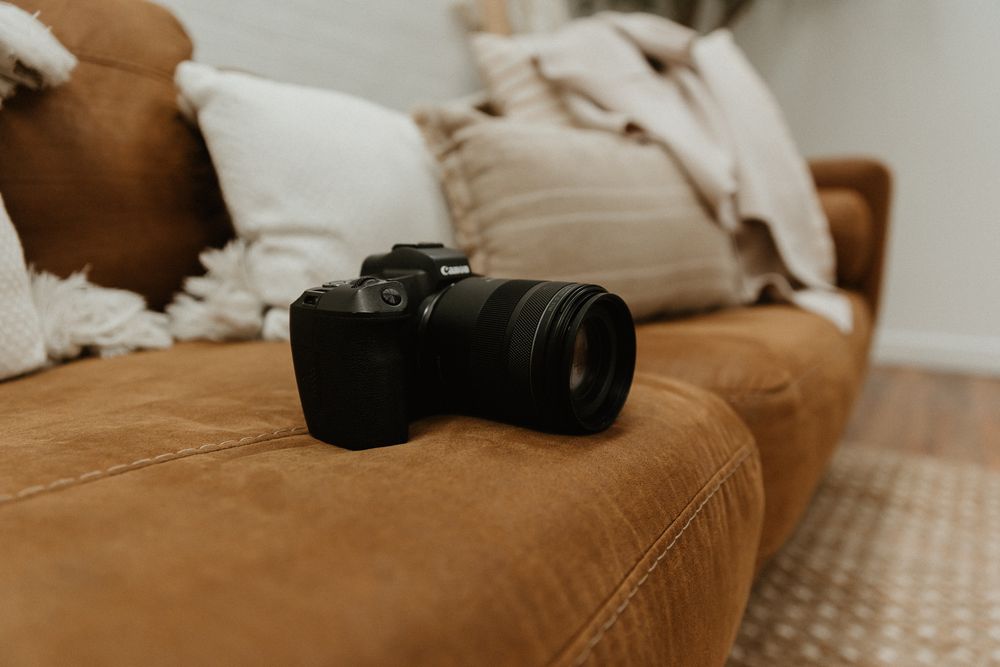 Camera equipment and laptop arranged on a tan couch with natural lighting.