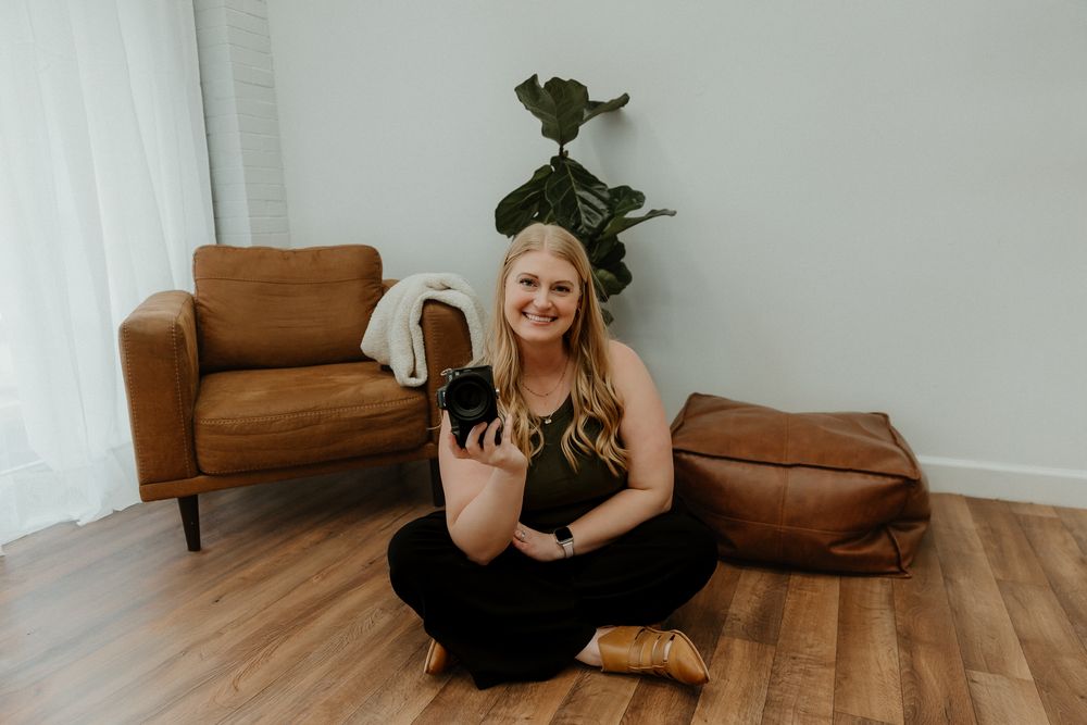 Person lounges comfortably on hardwood floor next to brown leather armchair in bright minimalist room.