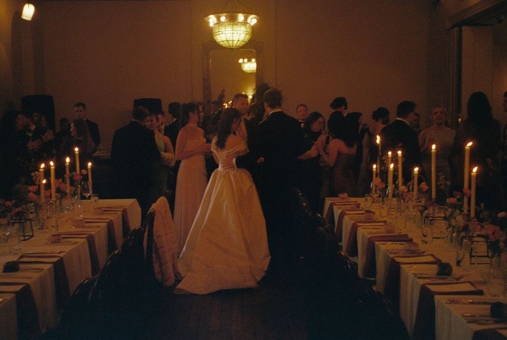 Bride and groom share first dance at candlelit wedding reception with elegantly set tables and guests in background.