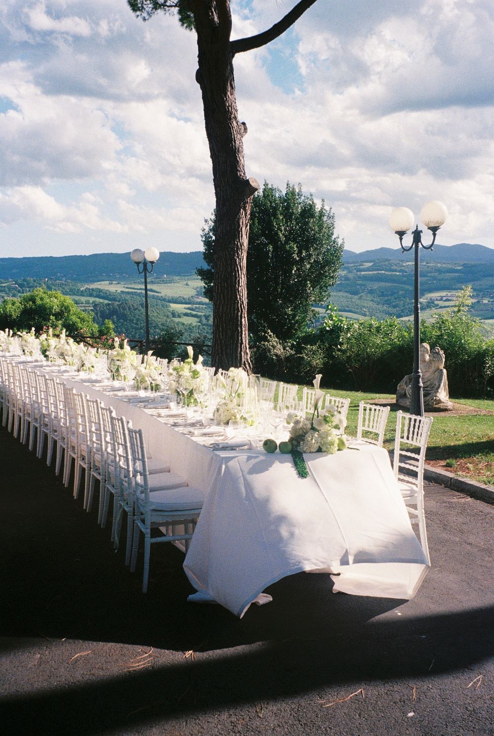 Elegant outdoor wedding reception with long white-draped tables and chiavari chairs overlooking a scenic Tuscan valley landscape.