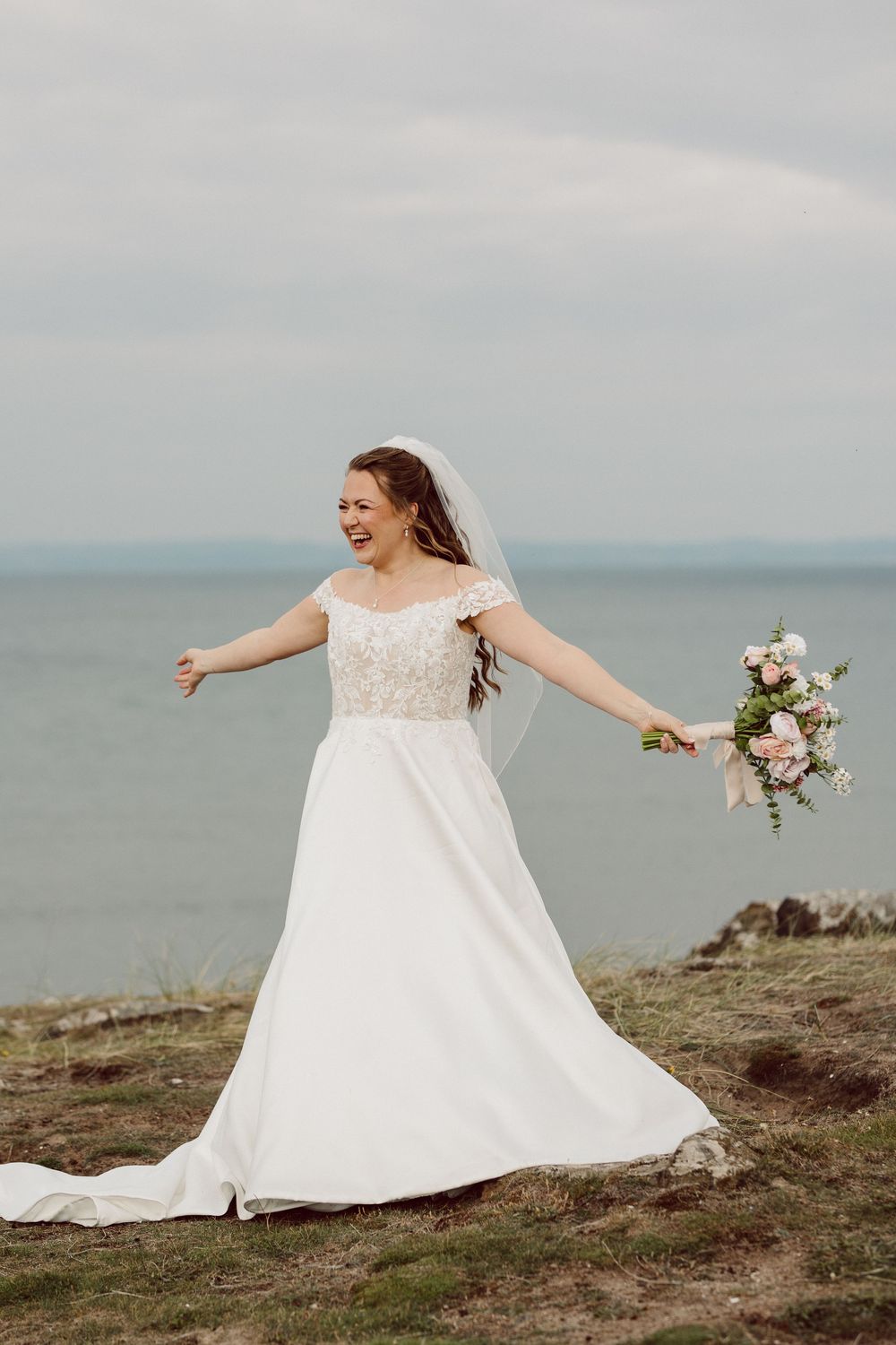 A joyful bride in a flowing white wedding dress twirls on a coastal cliff overlooking the ocean in three sequential photos.
