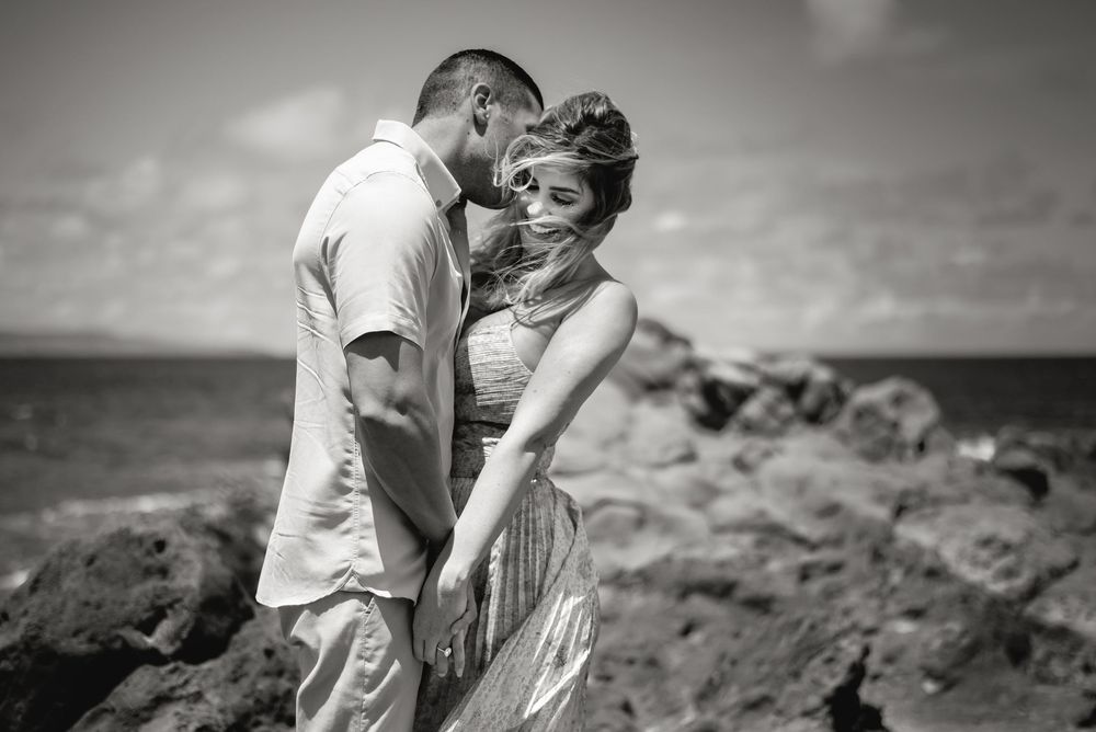 A couple shares an intimate moment against a dramatic coastal landscape at sunset.