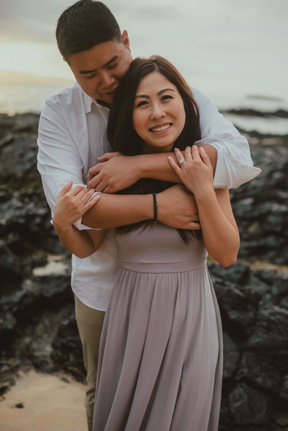 A tender embrace captured against a rocky coastal backdrop during sunset.