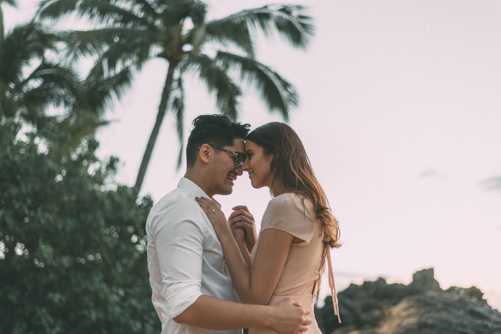 A romantic couple embraces under palm trees during a sunset photoshoot.