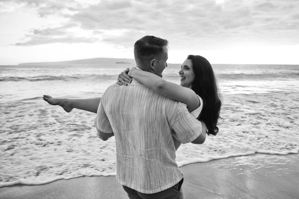 A couple dances together on a scenic beach with waves crashing behind them.