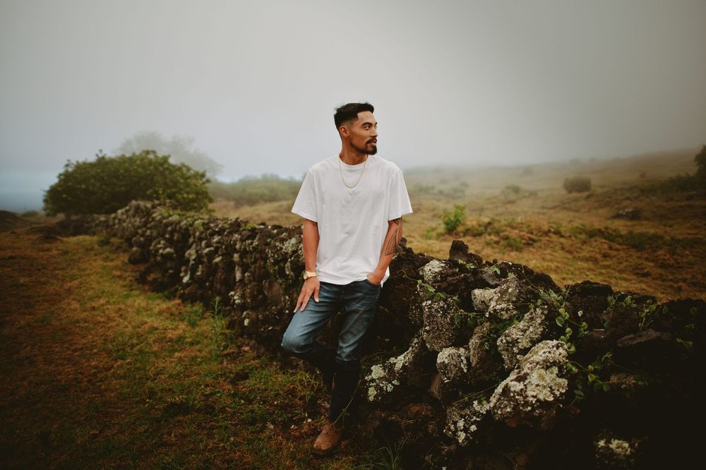 A person in white sits on rocky cliffs overlooking a misty mountainous landscape.