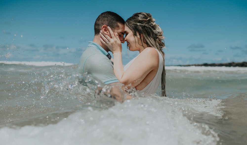 A couple plays and splashes in ocean waves on a sunny beach.