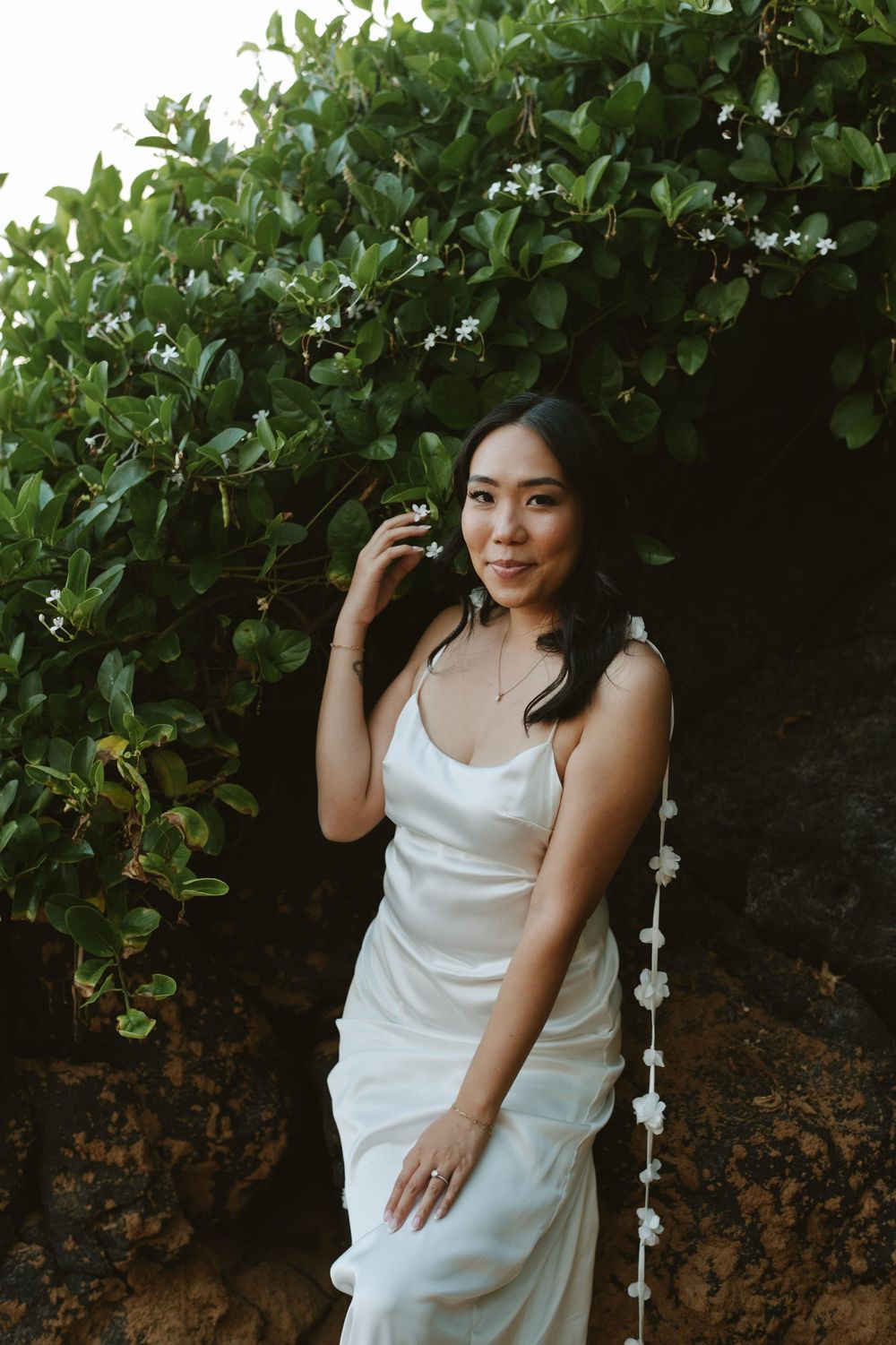 Woman in white dress poses against lush green foliage background during golden hour photoshoot.