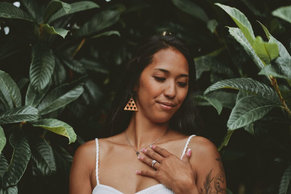 Woman in white top poses against lush tropical foliage background in artistic portrait.