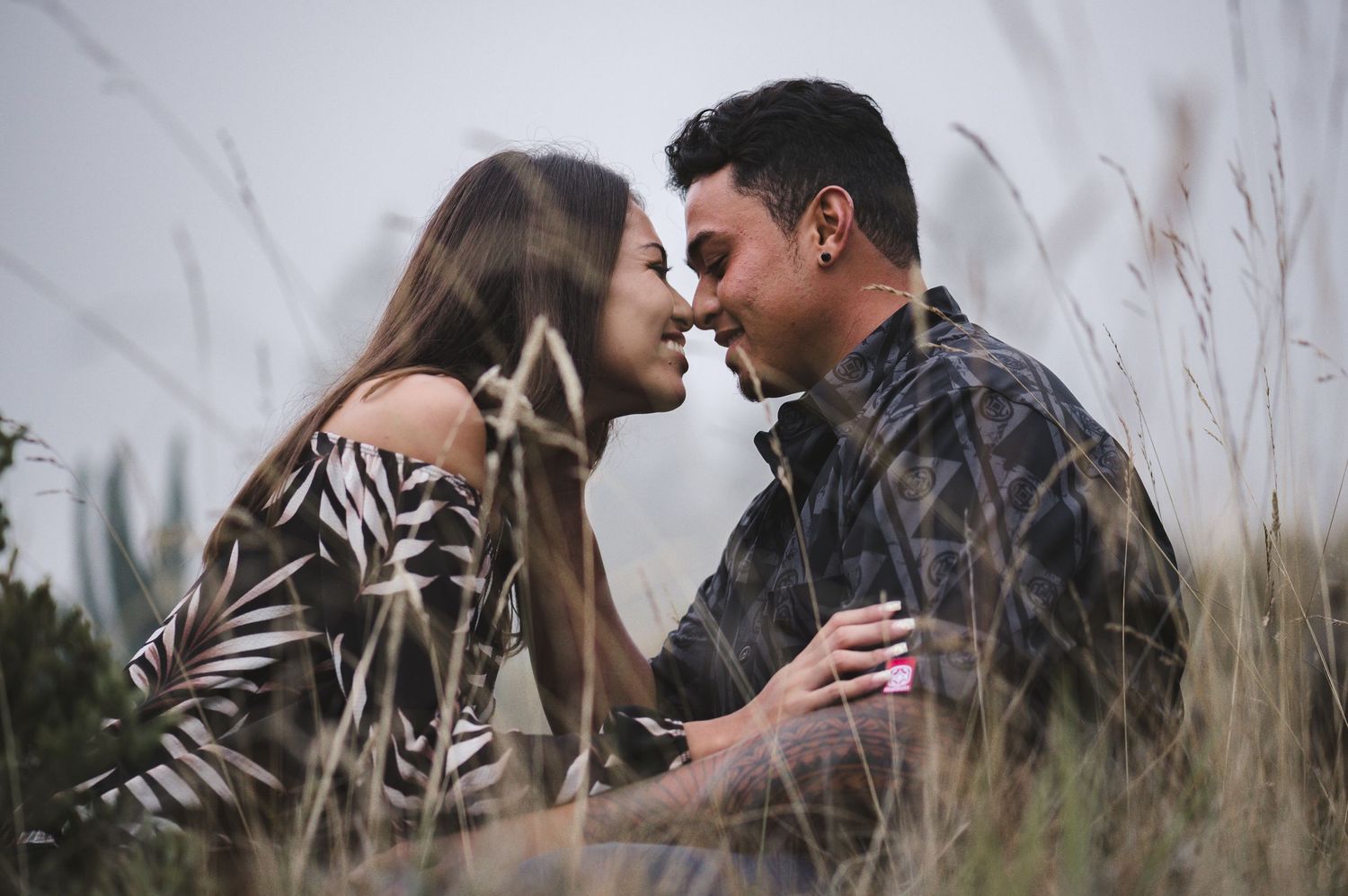 Intimate couple poses together in tall grass during golden hour.