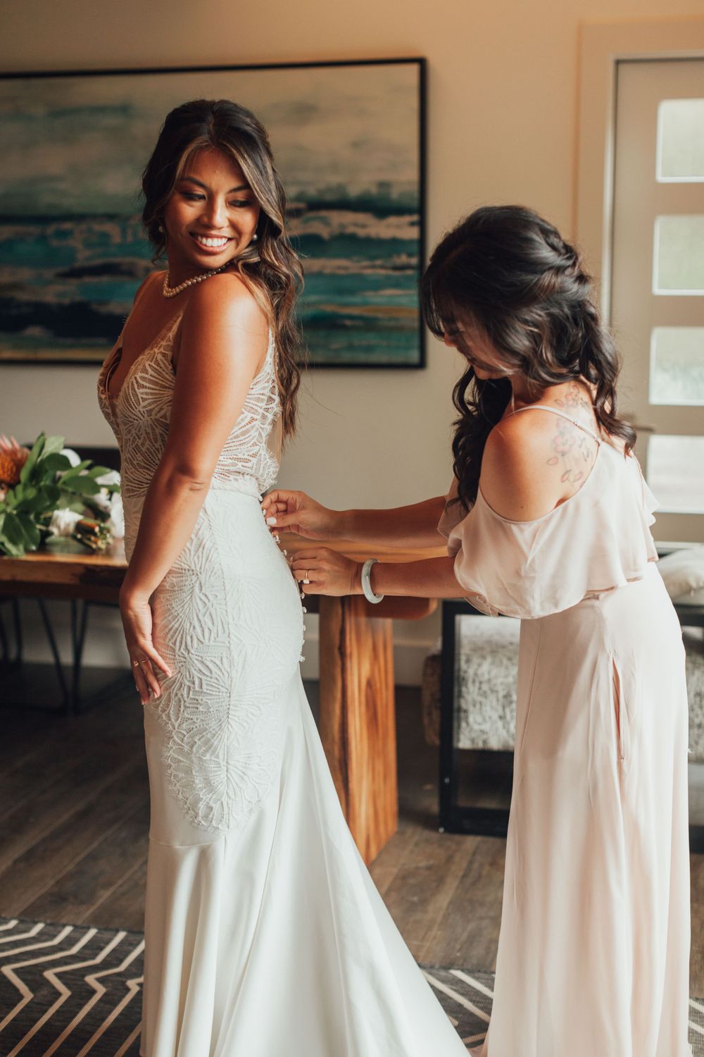 Wedding dress fitting moment captured in a room with coastal artwork and wooden furniture.