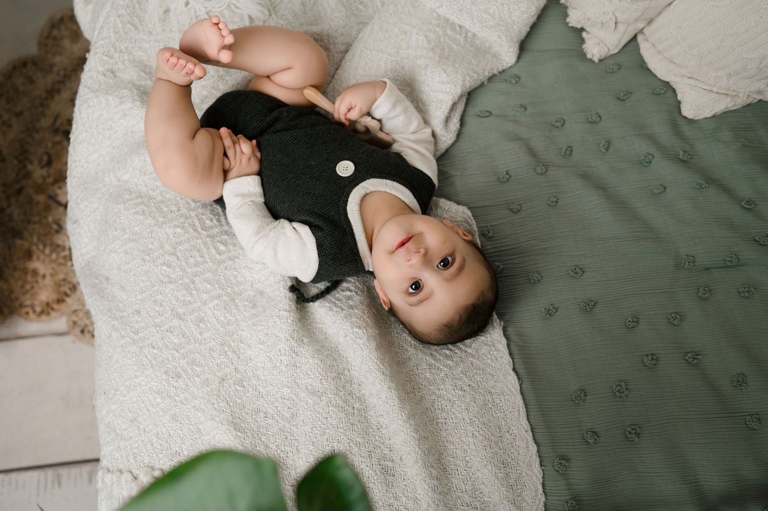 A person lies on a green velvet couch wearing a black top while looking upward in a relaxed pose.