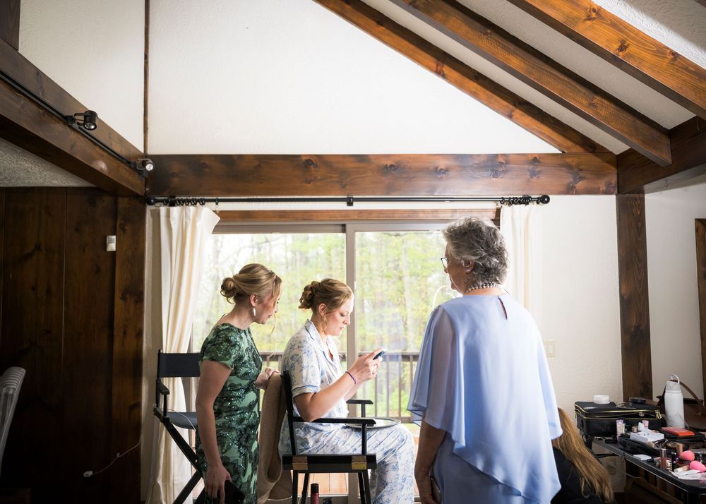 Three women conversing in a rustic wood-beamed room with natural light streaming through large windows.