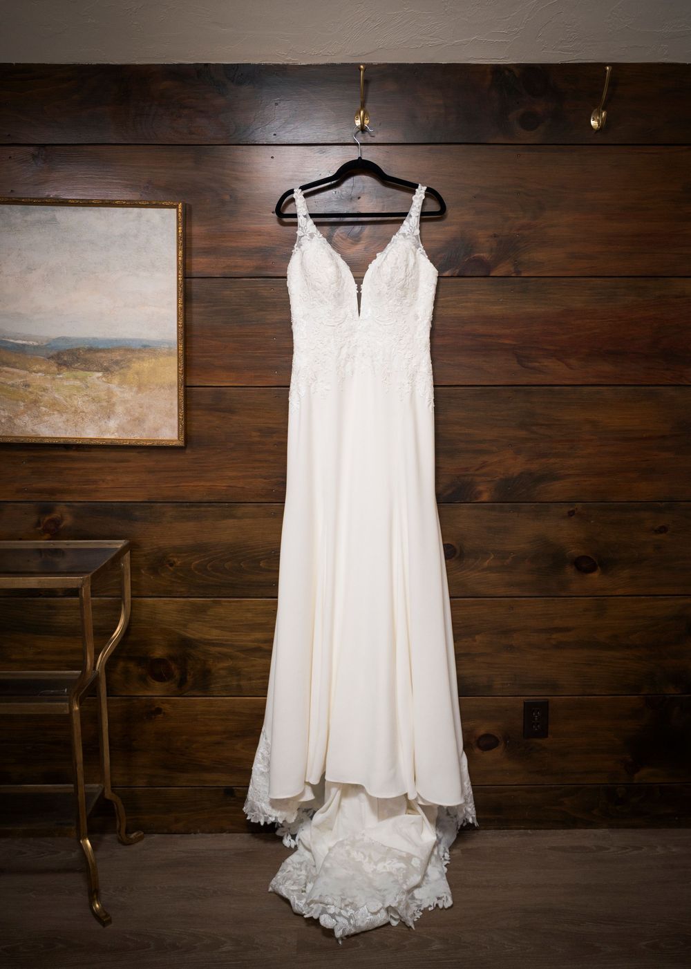 Elegant ivory wedding gown with lace bodice and train hanging on wooden wall.