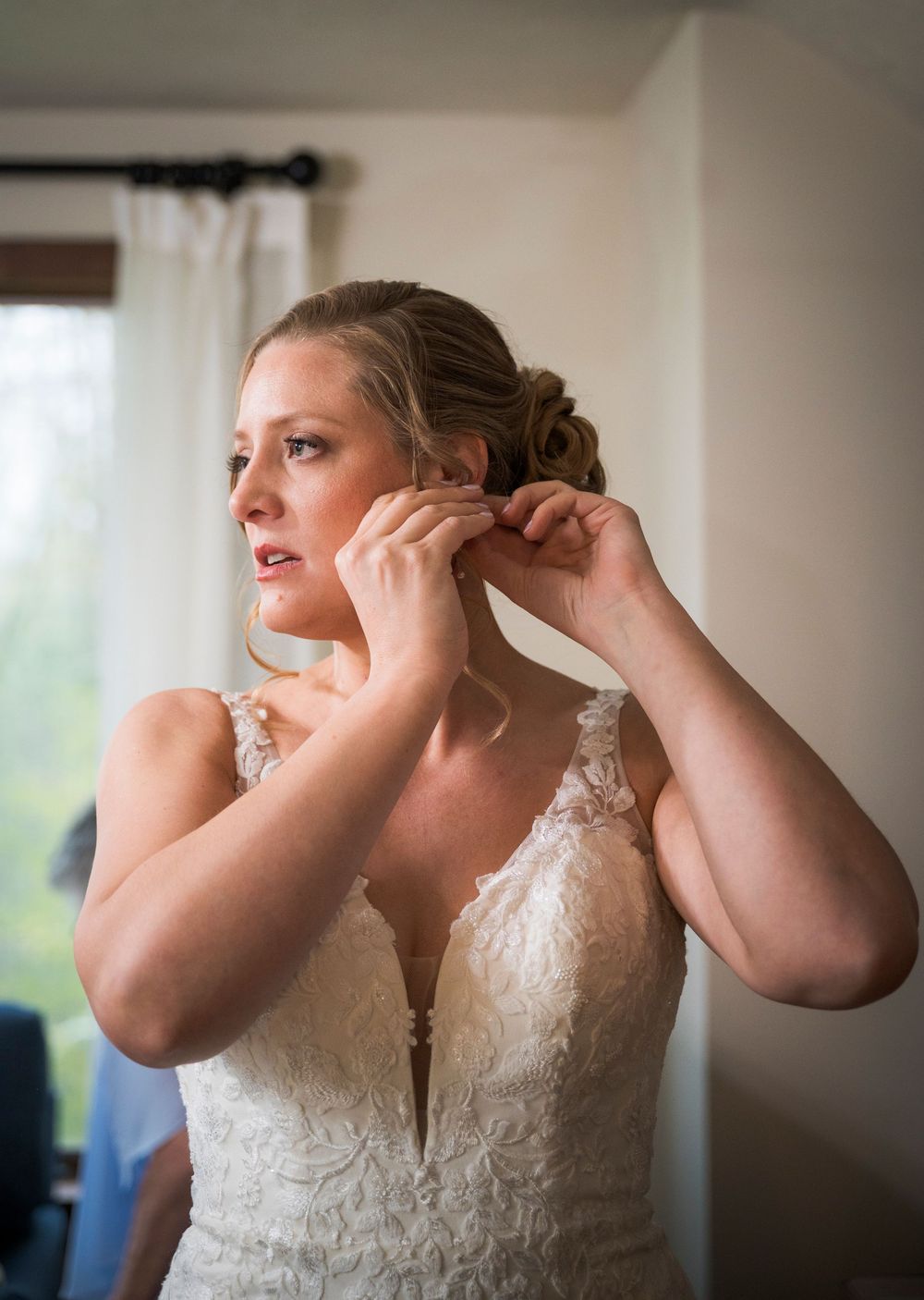 Bride in lace wedding gown putting on earrings while getting ready on her wedding day.