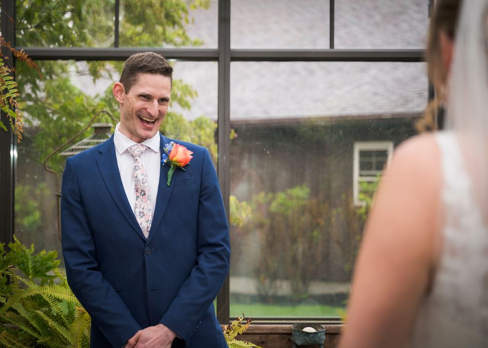 Groom in blue suit smiling joyfully as he sees bride for first time at wedding ceremony.
