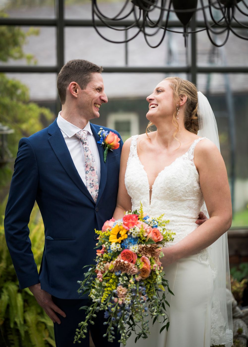 Smiling bride and groom sharing a joyful moment holding colorful wedding bouquet.