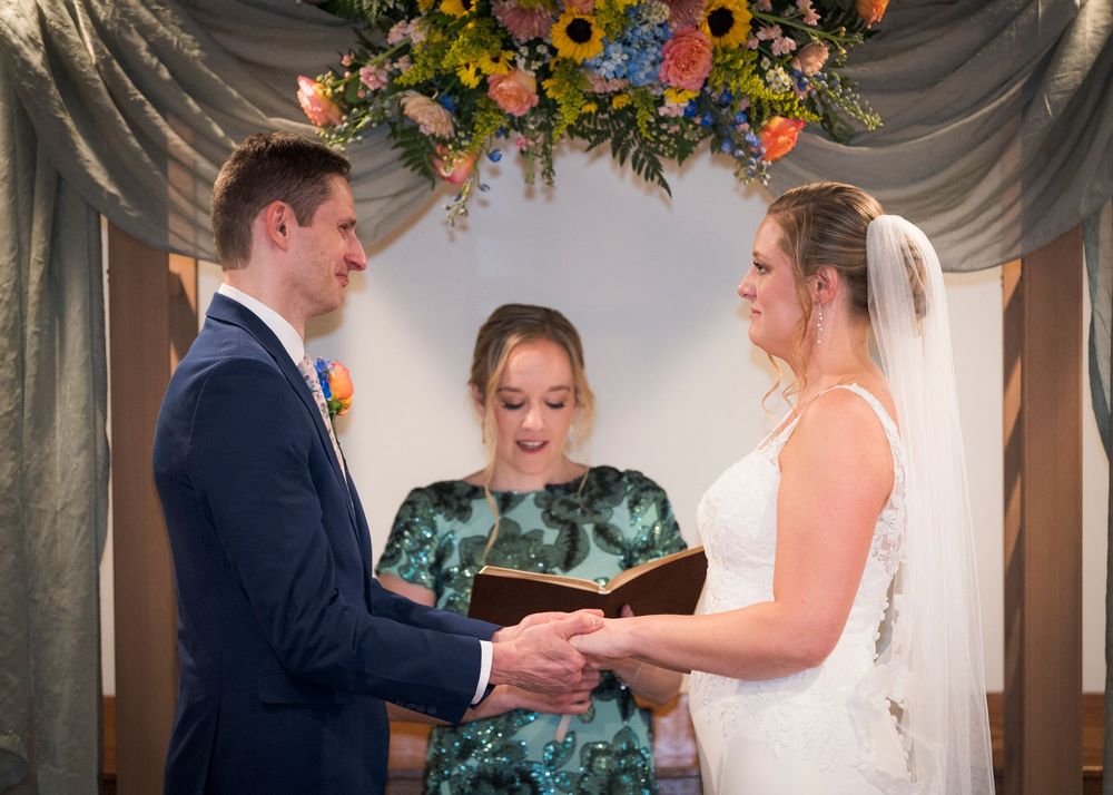 Bride and groom exchange vows with officiant during intimate wedding ceremony beneath floral arch.