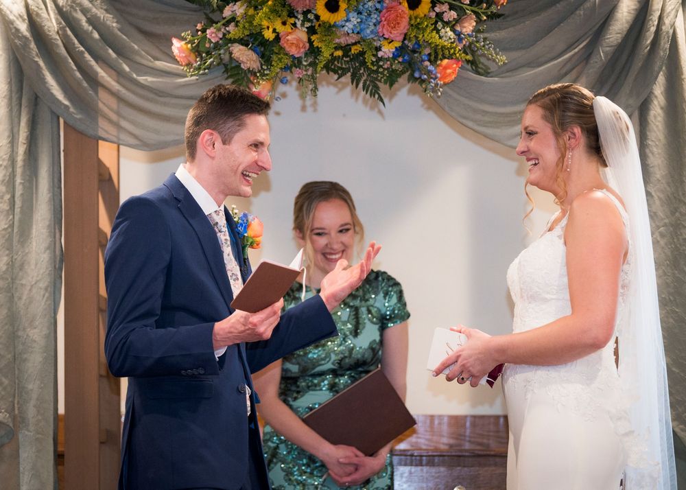 Bride and groom exchanging vows at wedding ceremony with officiant under floral arch.
