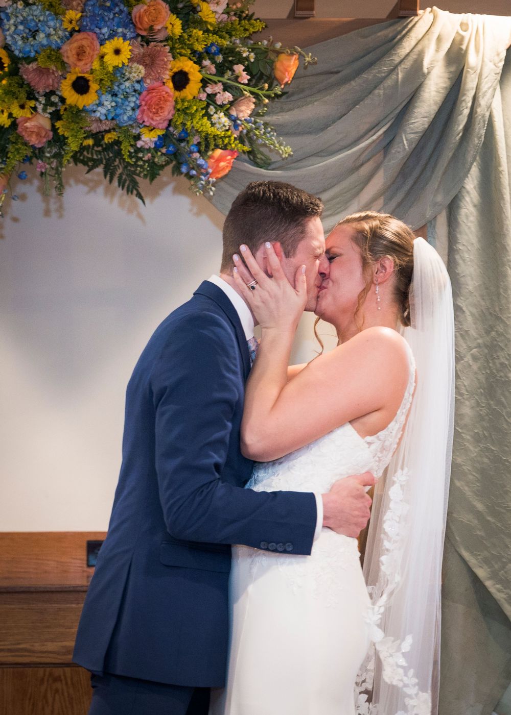 Bride and groom share their first kiss at the wedding altar adorned with colorful spring flowers.