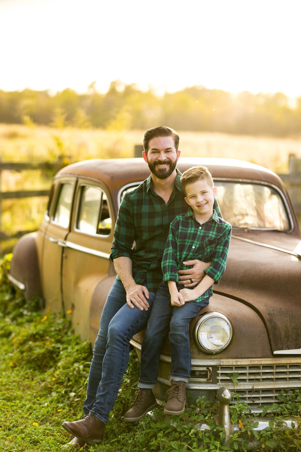 A rustic photoshoot featuring a vintage car and matching plaid shirts in golden sunset lighting.