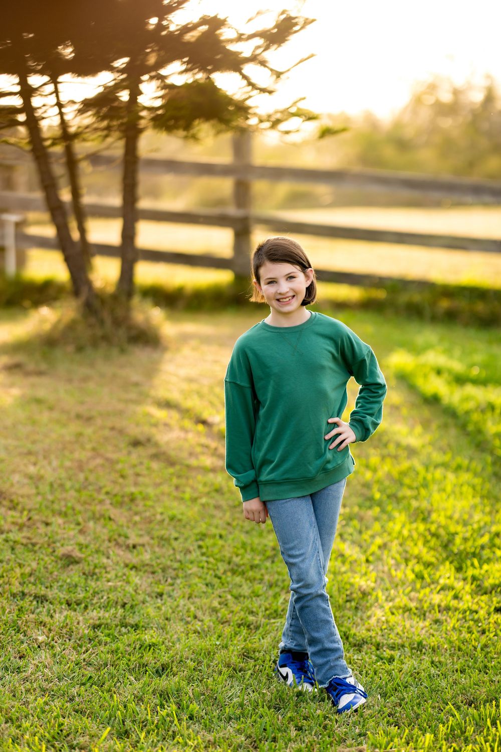 A person in a green sweater and jeans walks on grass during golden hour sunset in a park setting.