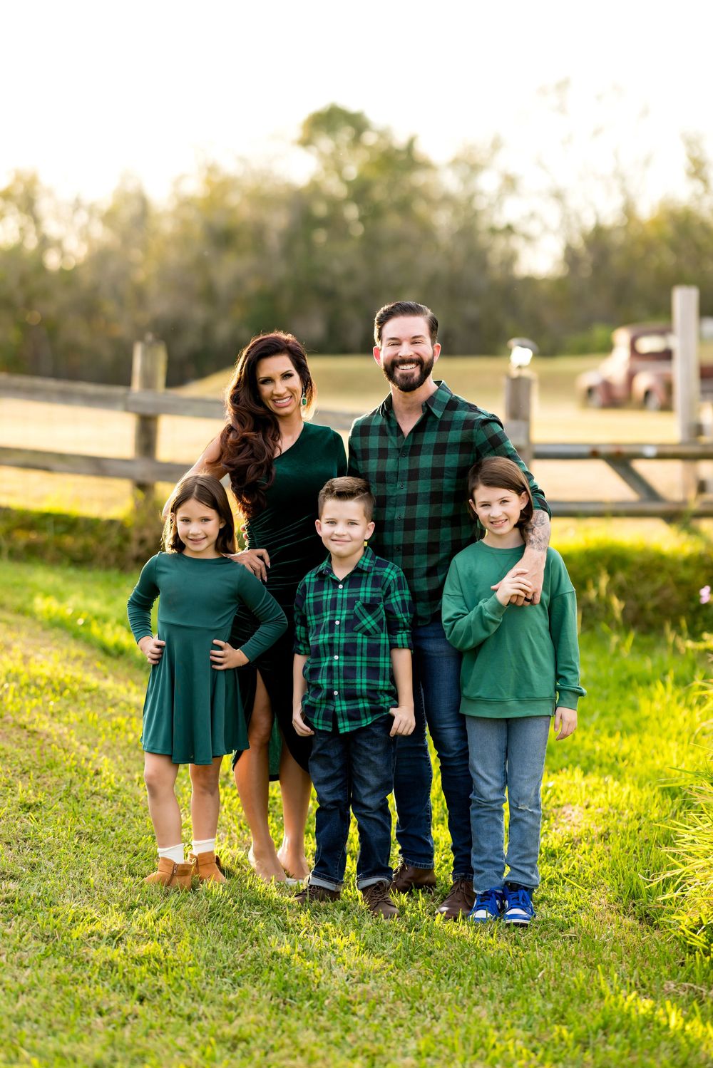 Family wearing coordinated green and plaid outfits poses together in a sunny meadow at golden hour.