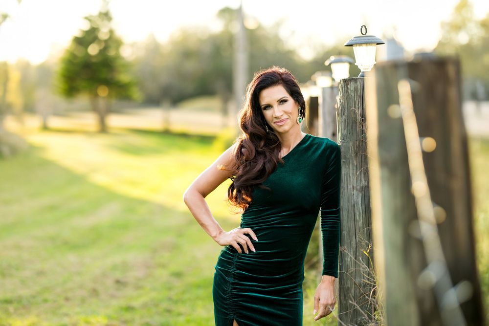 A woman in a dark green dress poses confidently outdoors during a golden hour photoshoot.